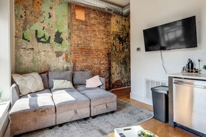 Ein Wohnzimmer mit Backsteinwand, grauem Sofa und einem Flachbildfernseher.