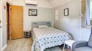 A bedroom with a bed, a chair, a small table, a wooden door, and an air conditioning unit. - Family Home + Guest House! Near Fishing, Boat Ramp (West Orange)