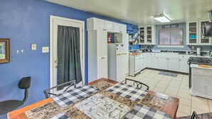 A compact kitchen with white cabinets, a dining area with a checkered tablecloth, and a blue wall. - Family Home + Guest House! Near Fishing, Boat Ramp (West Orange)
