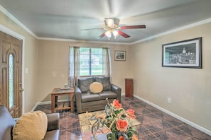 A living room with a brown leather couch, a coffee table with flowers, a ceiling fan, and a window with curtains. - Family Home + Guest House! Near Fishing, Boat Ramp (West Orange)