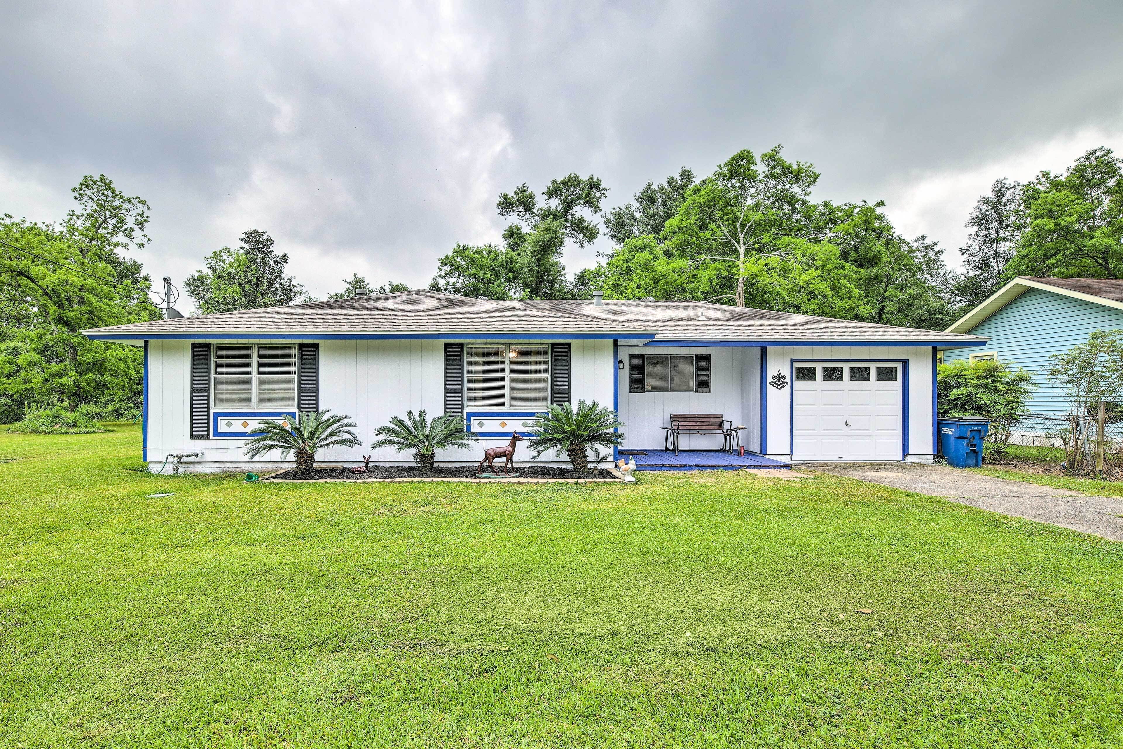 A single-story house with a garage, a front porch with a bench, and a small garden with palm trees.