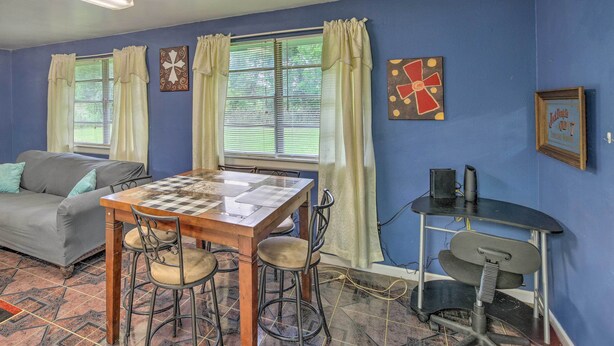 A room with a wooden dining table, four chairs, a sofa, and two windows with curtains. - Family Home + Guest House! Near Fishing, Boat Ramp (West Orange)