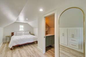 A bedroom with a bed, a small table, a window, and a bathroom with a sink and cabinets. - Mtn-View Deck w/ Grill! Modern Medicine Park Cabin (Medicine Park)