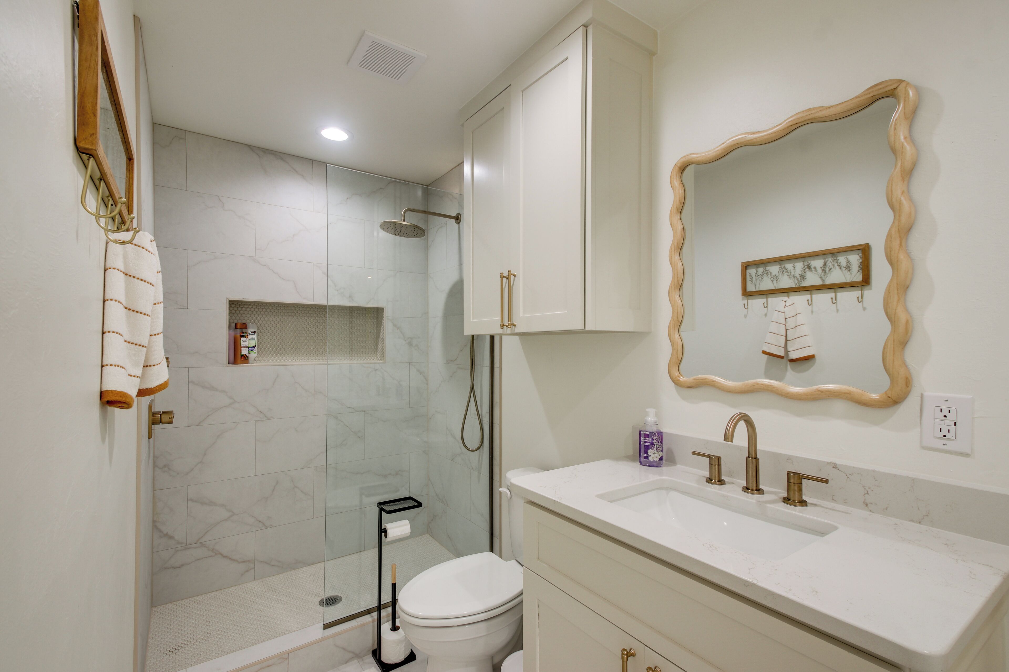 A bathroom with a shower, toilet, sink, and a mirror with a decorative frame.