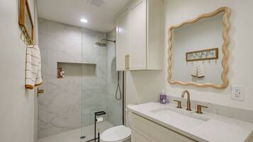 A bathroom with a shower, toilet, sink, and a mirror with a decorative frame.
