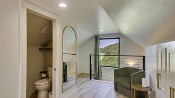 A bathroom with a toilet, a mirror, and a window with a view of greenery.