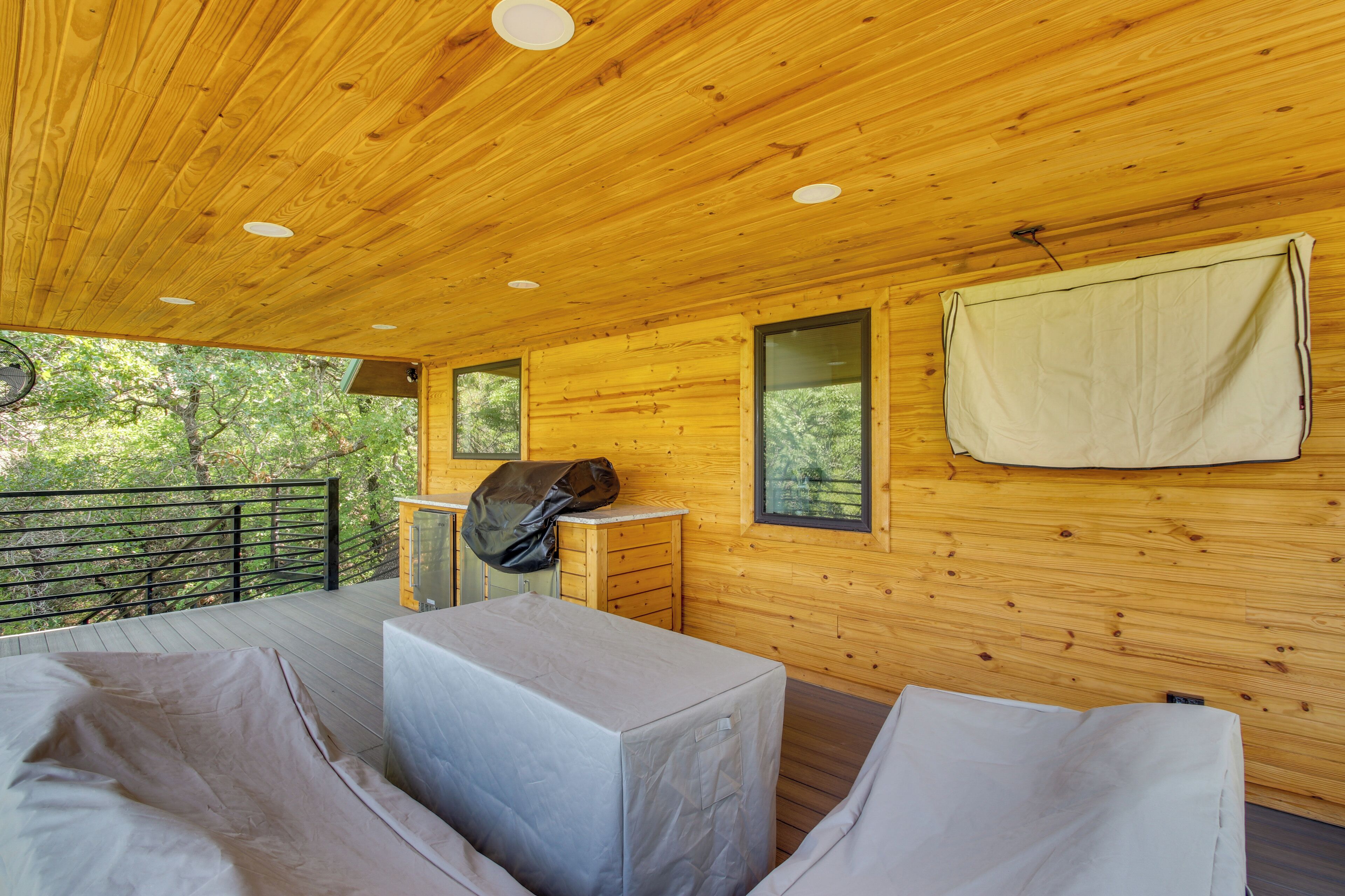 A wooden cabin with a balcony, a covered grill, and a window with a towel hanging.