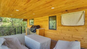 A wooden cabin with a balcony, a covered grill, and a window with a towel hanging.