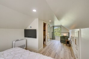 A bedroom with a bed, a flat-screen TV, a heater, and a window with a view of greenery. - Mtn-View Deck w/ Grill! Modern Medicine Park Cabin (Medicine Park)