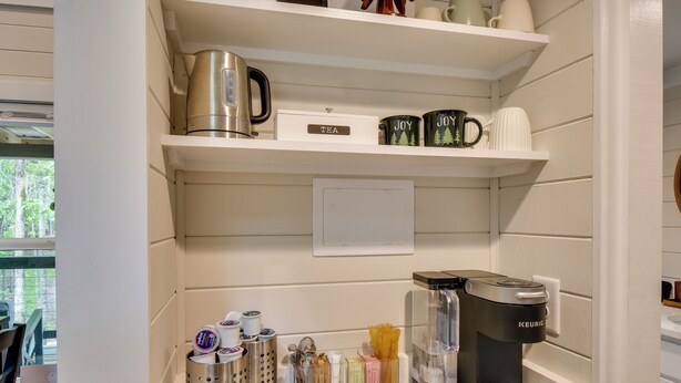 A kitchen with a coffee maker, tea kettle, and various kitchen utensils on shelves. - Tiny Home - Fire Pit, Grill, Deck & View! (Franklin)