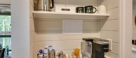 A kitchen with a coffee maker, tea kettle, and various kitchen utensils on shelves.