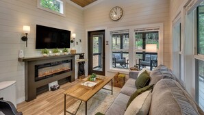A modern living room with a fireplace, a television, and a clock on the wall. - Tiny Home - Fire Pit, Grill, Deck & View! (Franklin)