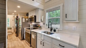 A modern kitchen with stainless steel appliances, a built-in oven, and a window with a view of the outdoors. - Tiny Home - Fire Pit, Grill, Deck & View! (Franklin)