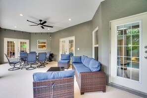 A spacious patio with a ceiling fan, a seating area with blue cushioned chairs and sofas, and a large sliding glass door leading to a garden. - Heated Pool & Lanai Cookouts! Cape Coral Getaway (Cape Coral)