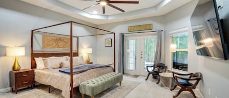 A bedroom with a four-poster bed, a sitting area with chairs, a television, and a ceiling fan.