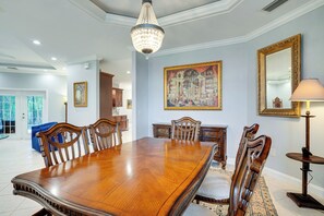 A dining room with a large wooden table, ornate chairs, a chandelier, and a large framed painting on the wall. - Heated Pool & Lanai Cookouts! Cape Coral Getaway (Cape Coral)