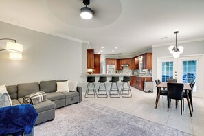 Ein modernes Wohnzimmer mit grauem Sofa, einem gemusterten Teppich und einem Essbereich mit Tisch und Stühlen.
