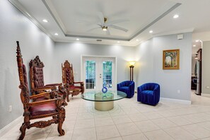 A spacious living room with a glass coffee table, ornate wooden chairs, and a modern blue sofa. - Heated Pool & Lanai Cookouts! Cape Coral Getaway (Cape Coral)