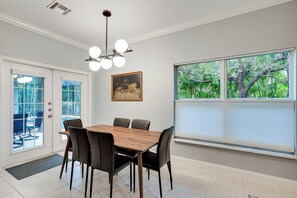 A dining area with a wooden table and black chairs, a ceiling light fixture, a painting on the wall, and a window with blinds. - Heated Pool & Lanai Cookouts! Cape Coral Getaway (Cape Coral)