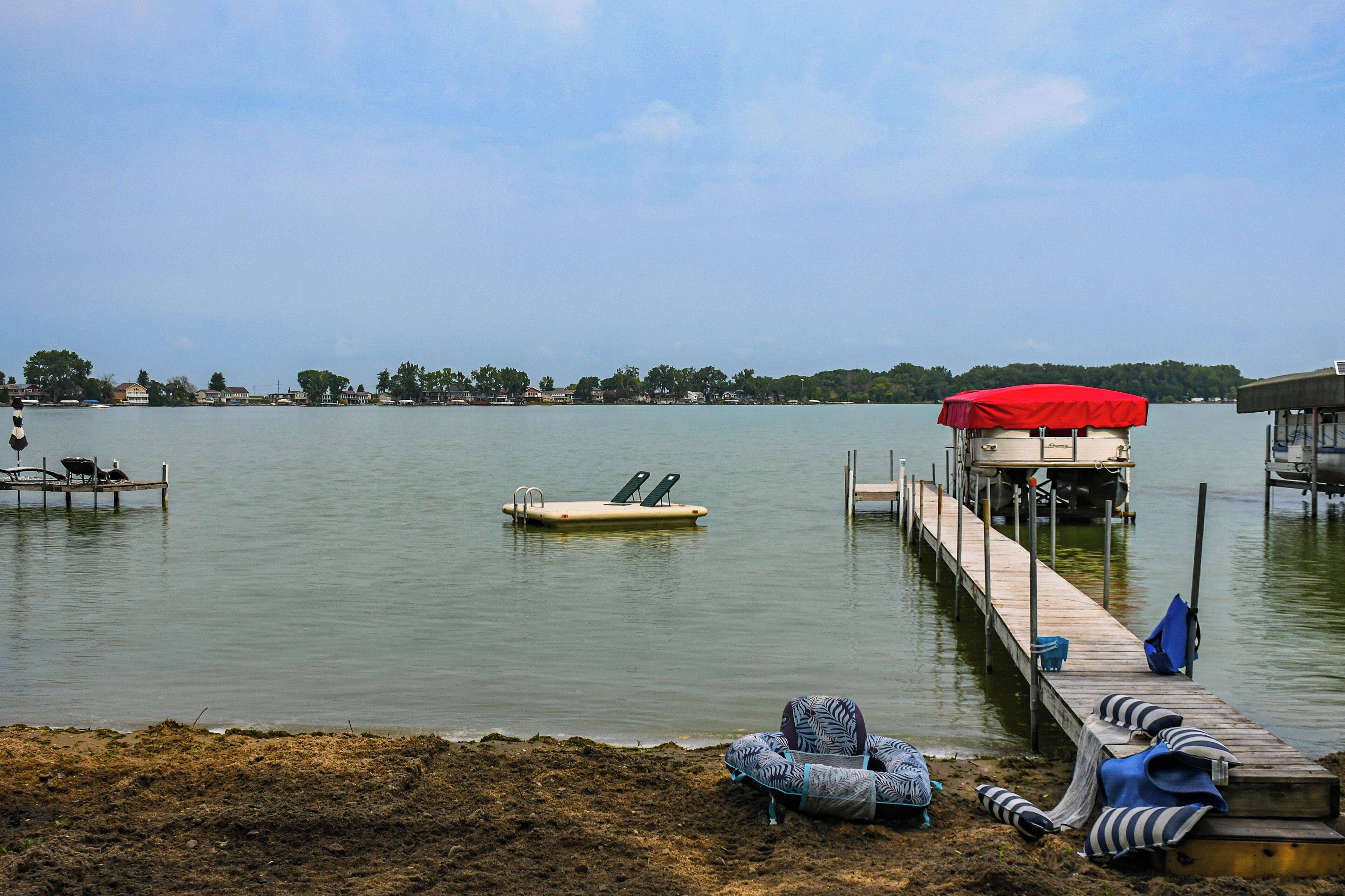 Un muelle junto al lago con toldo rojo, sillas de descanso y un bote pequeño.