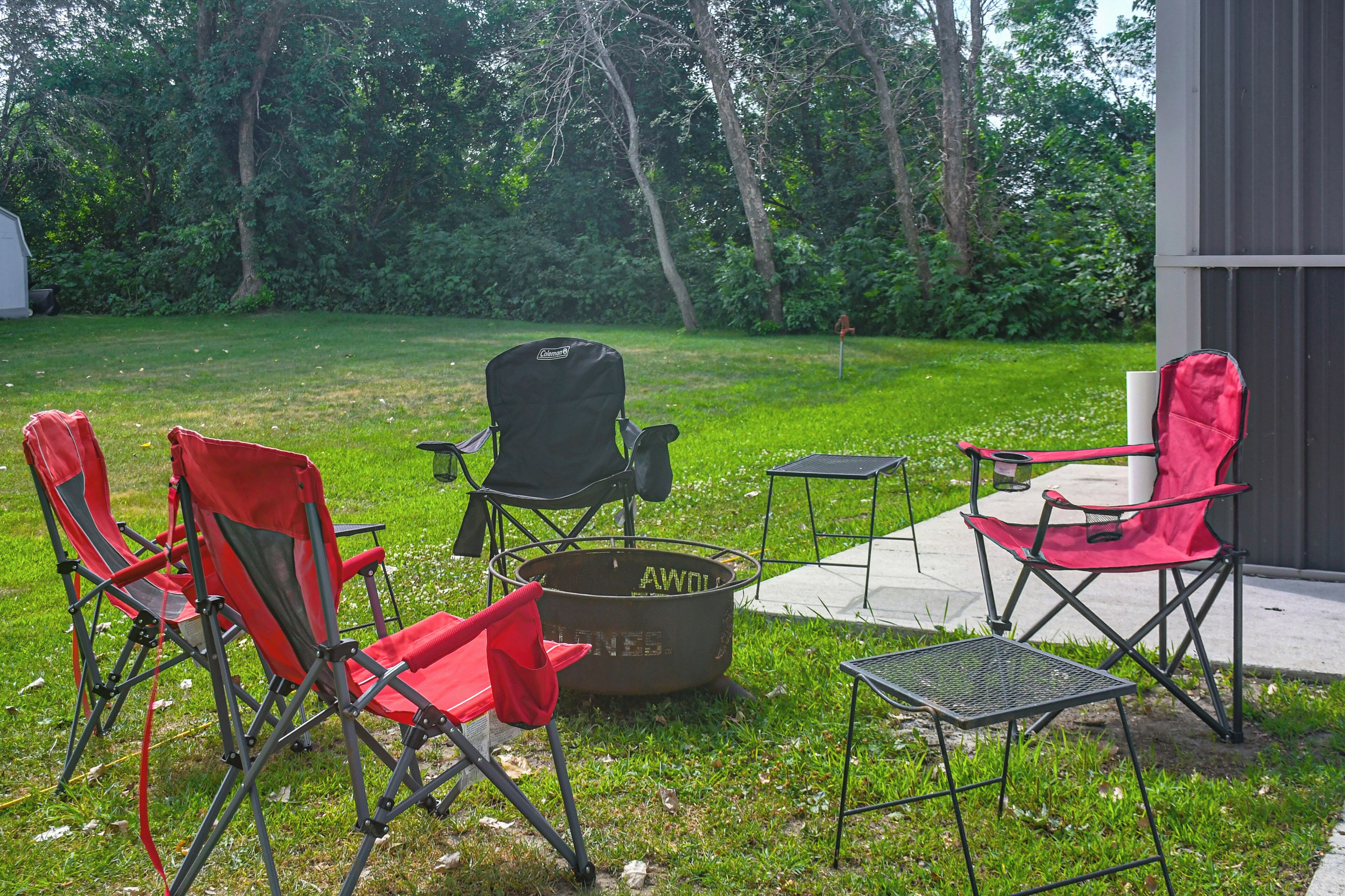 Un espace extérieur aménagé avec trois chaises pliantes rouges, une chaise Coleman noire et une table en métal.