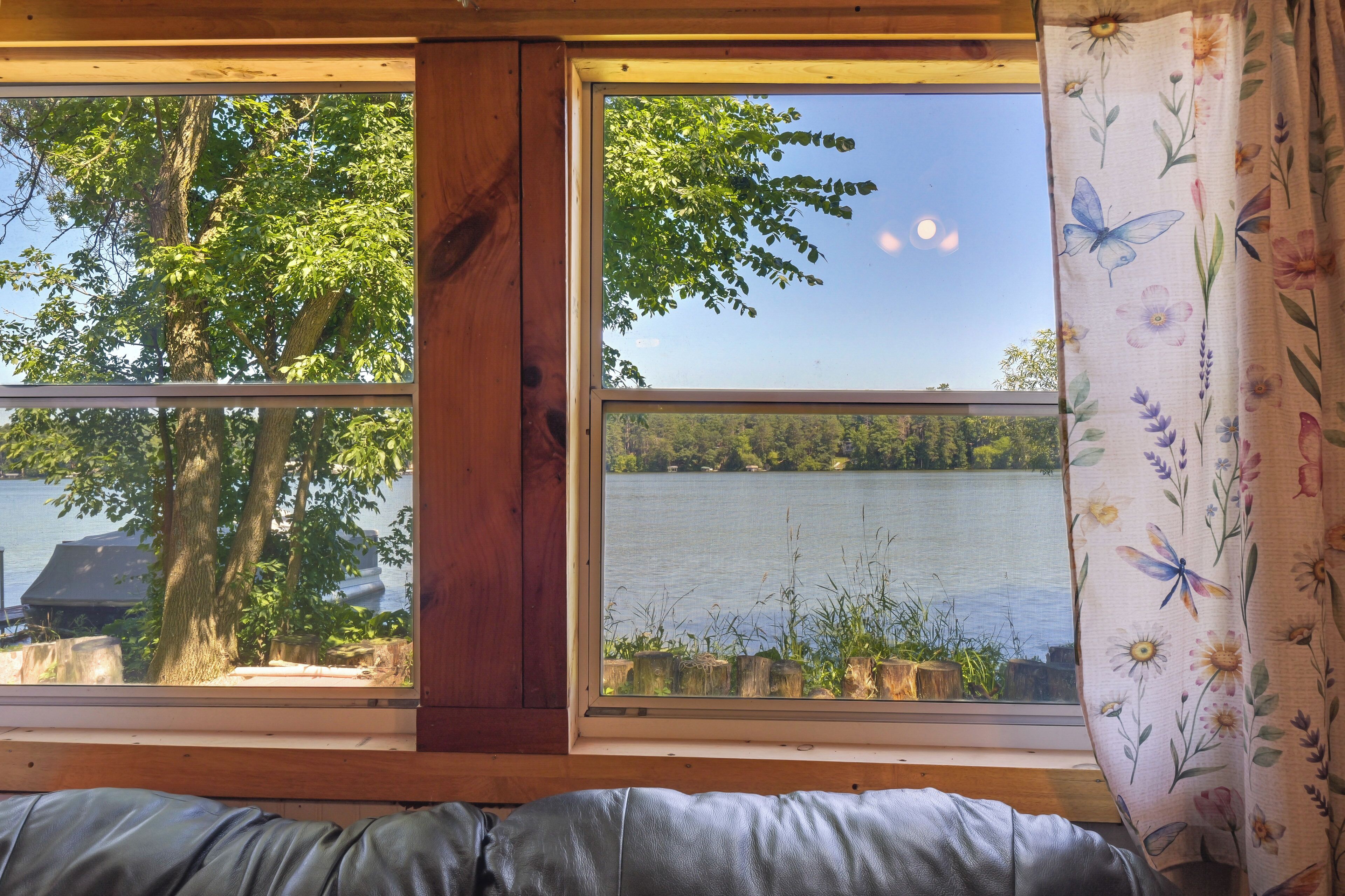 A room with a large window overlooking a lake, a wooden beam structure, and a view of trees and a boat.
