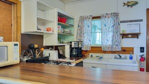 A kitchen with a microwave, stove, sink, and various kitchen utensils. There is a window with floral curtains and a fish decoration on the wall. - Pet-Friendly Rustic Cabin Steps from Lake Chetek (Chetek)