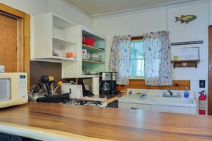 A kitchen with a microwave, stove, sink, and various kitchen utensils. There is a window with floral curtains and a fish decoration on the wall. - Pet-Friendly Rustic Cabin Steps from Lake Chetek (Chetek)