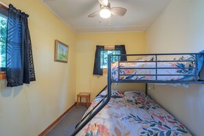 A dormitory room with bunk beds, a ceiling fan, a small wooden stool, and a framed picture on the wall.