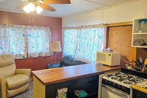 A compact kitchen with a stove, microwave, and a small dining area with a chair and table. - Pet-Friendly Rustic Cabin Steps from Lake Chetek (Chetek)