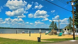 A beach with a volleyball net, playground equipment, and a lake in the background. - Pet-Friendly Rustic Cabin Steps from Lake Chetek (Chetek)