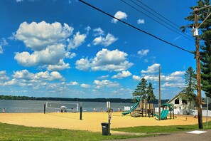 A beach with a volleyball net, playground equipment, and a lake in the background. - Pet-Friendly Rustic Cabin Steps from Lake Chetek (Chetek)