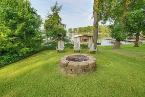 A lakeside outdoor seating area with a fire pit and Adirondack chairs.