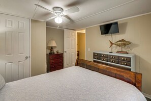 Une chambre à coucher comprenant un lit, une commode, un téléviseur et un ventilateur de plafond.