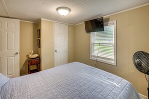 A bedroom with a bed, a TV mounted on the wall, a window with blinds, and a standing fan. - Dock & Outdoor Bar! Lake Blackshear Getaway (Cobb)