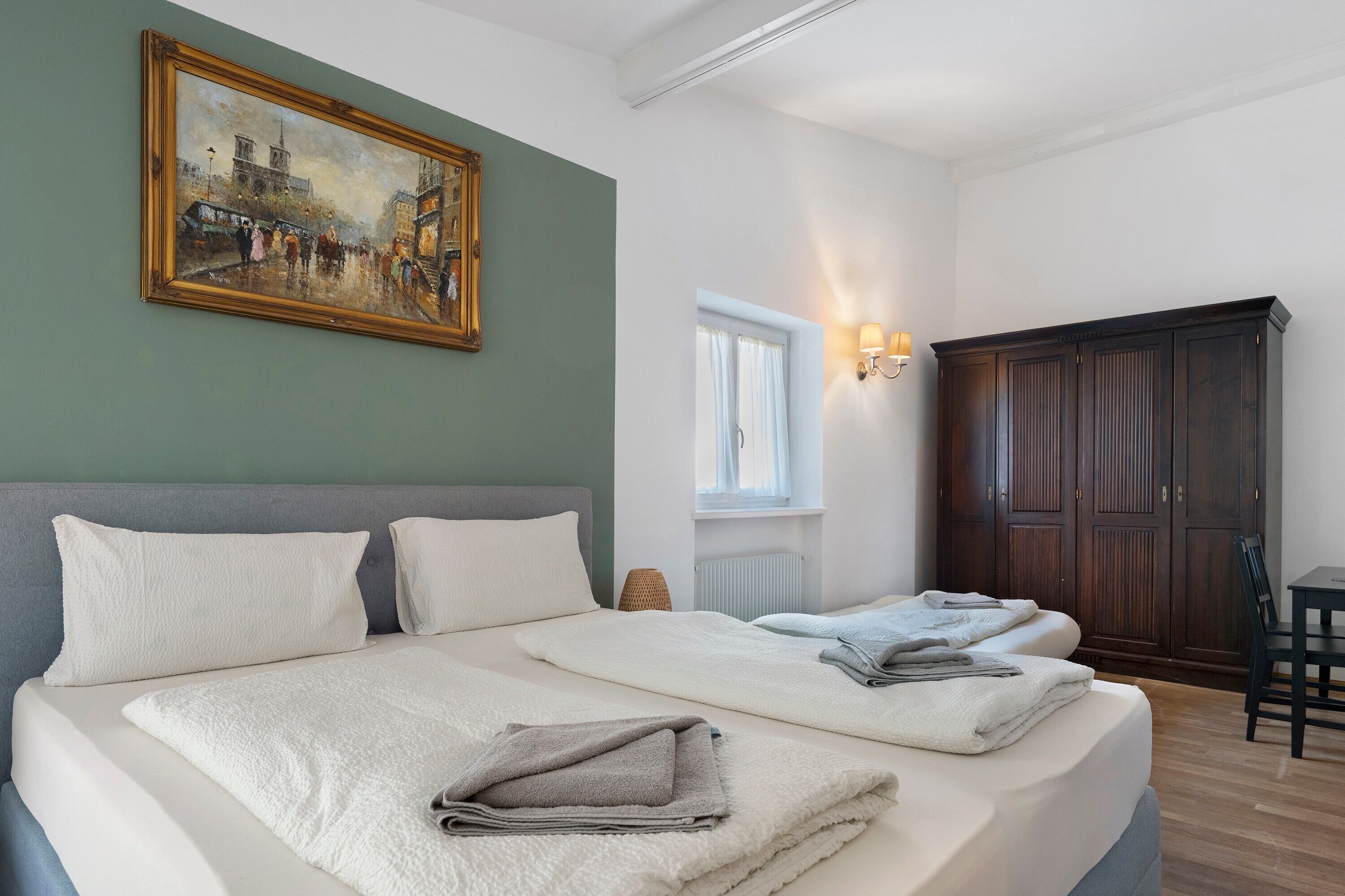 Una habitación de hotel con una cama grande, un cuadro en la pared, un armario y una ventana con cortinas.