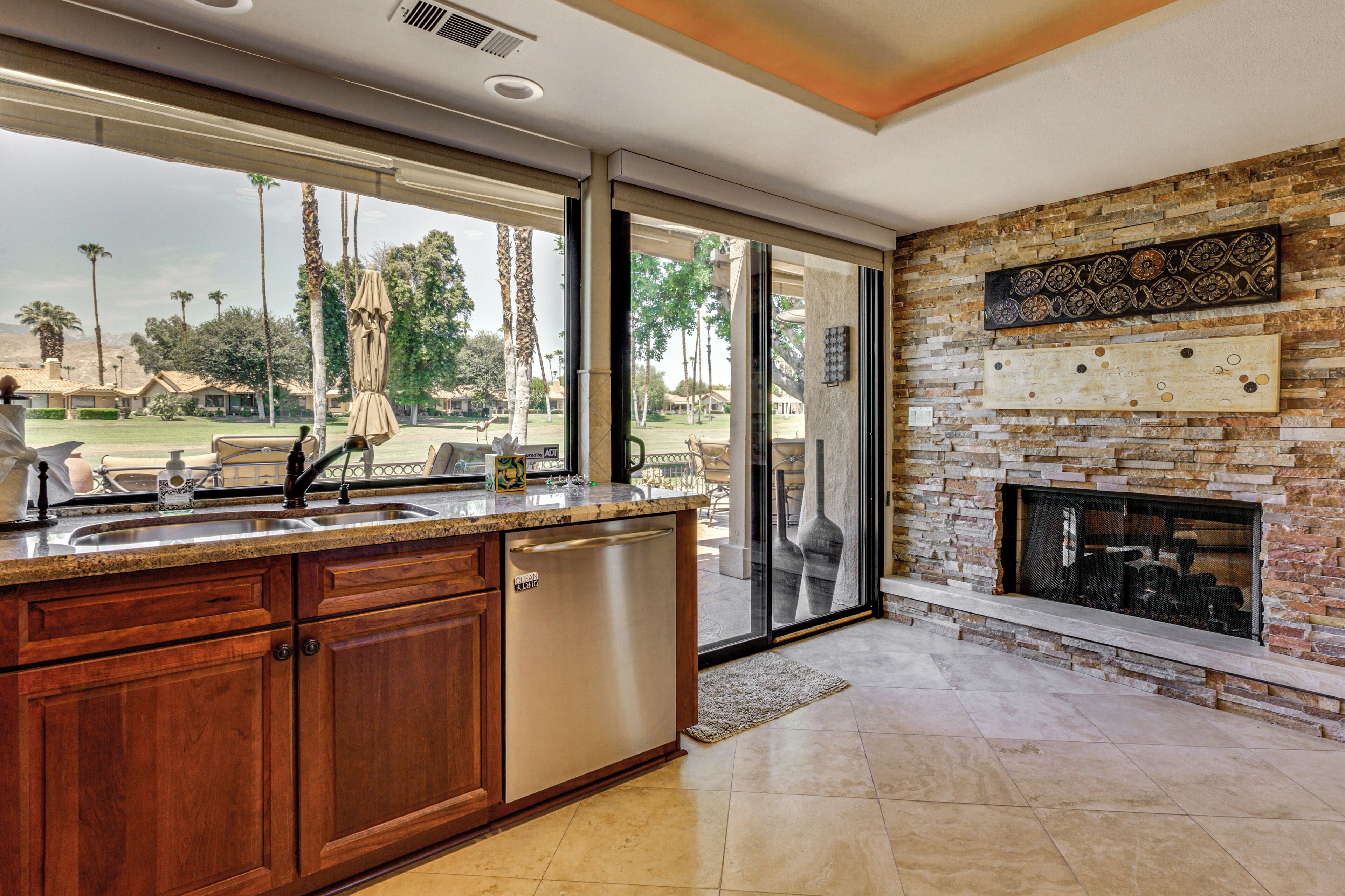 Una cocina moderna con lavavajillas integrado, un amplio ventanal con vistas a un jardín ajardinado y una chimenea de piedra.