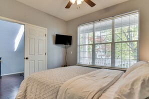 Ein Schlafzimmer mit einem Bett, einem an der Wand montierten Fernseher, einer Tür und einem Fenster mit Jalousien.