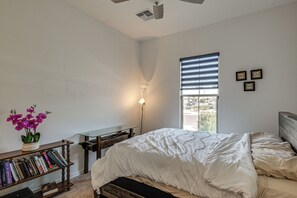 Ein Schlafzimmer mit Bett, Nachttisch, Lampe, Fenster mit Jalousien, Bücherregal und einer Wand mit inspirierenden Sprüchen in Rahmen.