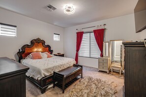 Une chambre à coucher avec un lit en bois, une table de chevet, une commode, un miroir et une fenêtre avec des rideaux rouges.