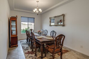 Een eetkamer met een houten tafel gedekt voor zes personen, omringd door sierlijke stoelen, een kroonluchter en een grote spiegel aan de muur.