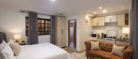 A hotel room with a bed, a sofa, a small table with a plant, and a kitchenette.