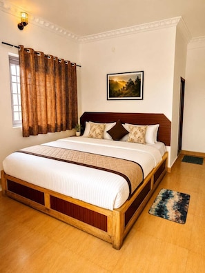 A bedroom with a wooden bed, a painting on the wall, and a window with curtains. - Aura Castle (Kodaikanal)