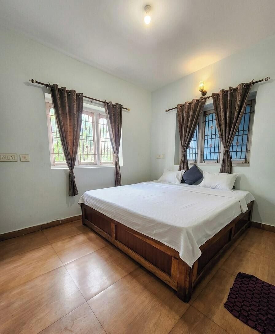 A bedroom with a wooden bed, two windows with curtains, a light fixture, and a tiled floor.
