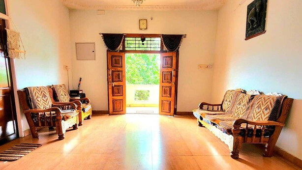 A spacious living room with a wooden floor, two sofas with patterned cushions, a wooden door with glass panels, and a chandelier.