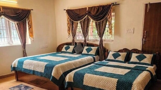 A room with two beds, each with a quilted bedspread, a wooden headboard, and a window with curtains. - Aura Castle (Kodaikanal)