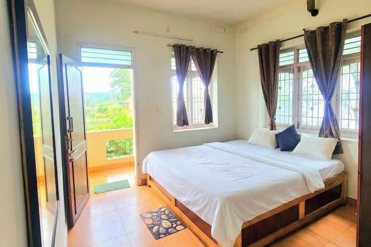 A bedroom with a single bed, a window with curtains, a door leading to a balcony, and a small rug on the floor.