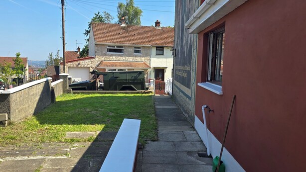 A narrow alleyway with a parked military vehicle, a green lawn, and a red building. - BridAj's Place is a full Semi-detached 3 Bed home with parking full of History. (Belfast)