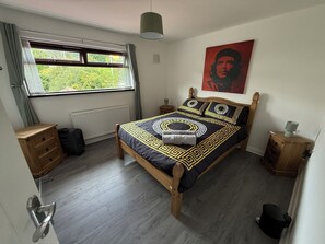 A bedroom with a bed, a window, a radiator, a wooden dresser, a bedside table, and a wall with a poster. - BridAj's Place is a full Semi-detached 3 Bed home with parking full of History. (Belfast)