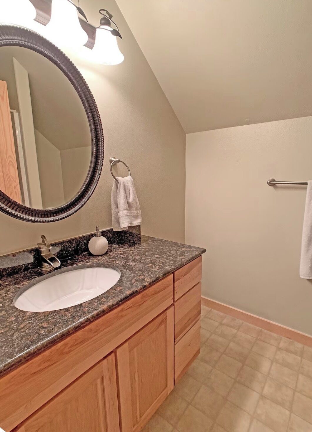 A bathroom with a granite countertop, a white sink, wooden cabinets, a large mirror, and a towel rack.